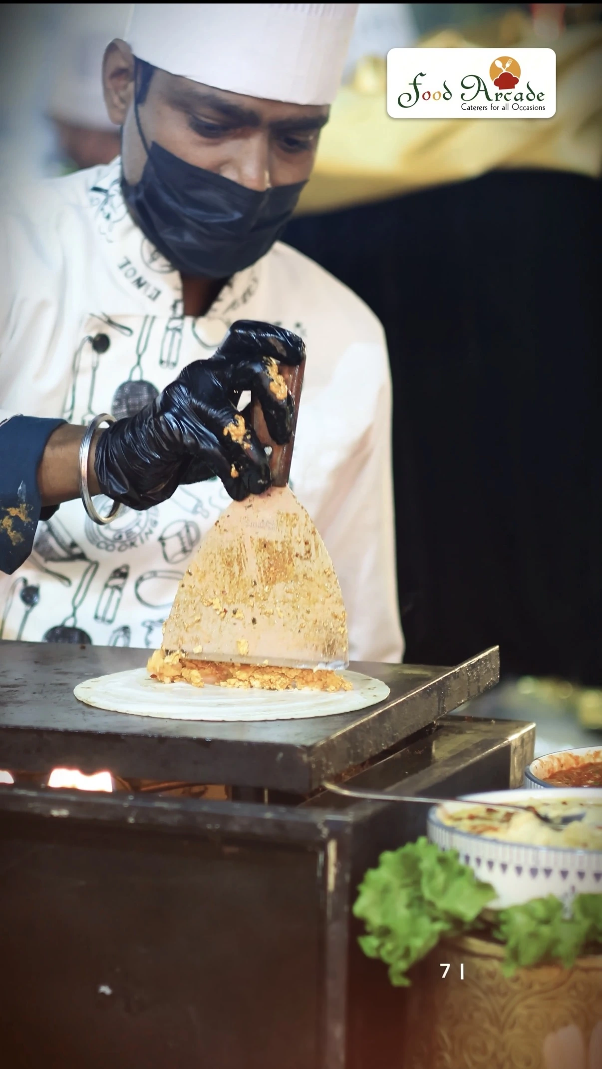 Chef in whites preparing a filled flatbread on a hot plate at a live counter