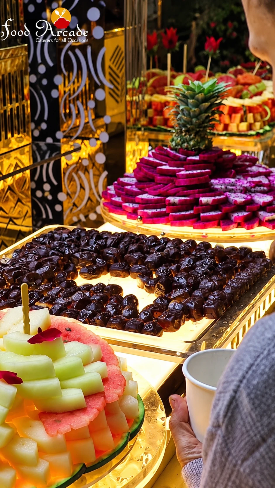 Illuminated trays of dragon fruit slices, dates and melon with a pineapple crown