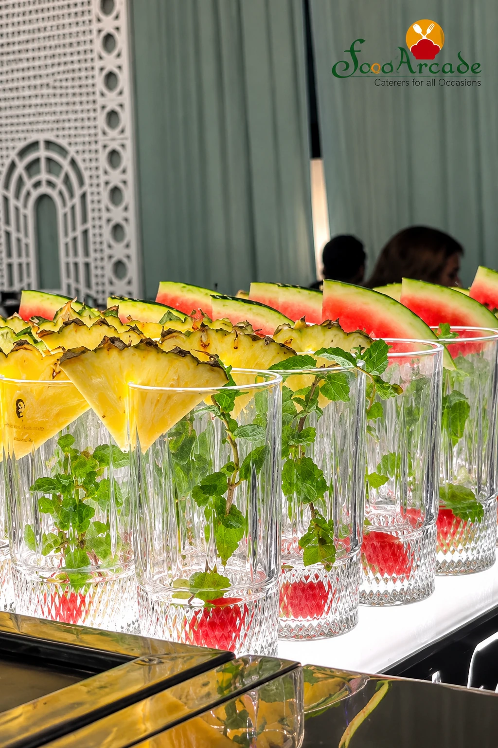 Row of glasses with mint, pineapple and watermelon garnish on a lit counter