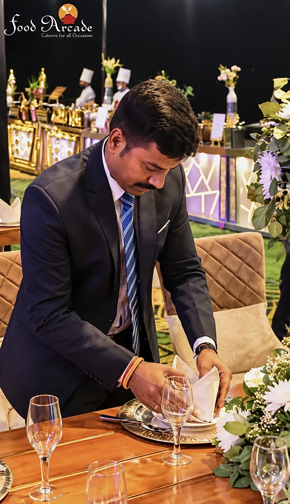 Man in a suit folding a napkin on a laid table at an event
